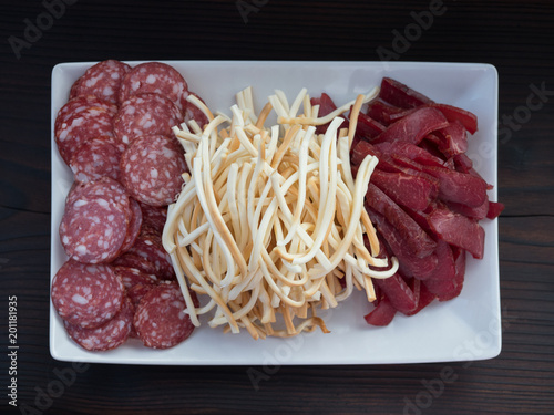 sausage, cheese, meat on white plate, on dark background
