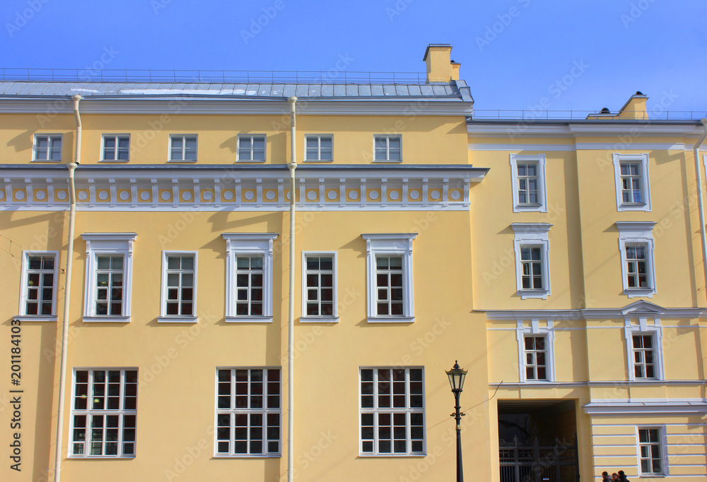 Building Facade of Old Historic House Built in Minimalist Architecture Style and Painted in Soft Yellow Color. Building Exterior Design and Elements Front View with Classical Square Frame Windows.