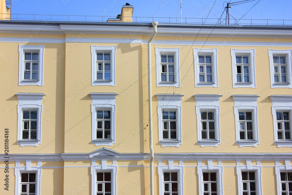 Obraz premium Architecture Detail of Old Historical Building Front. Classical Minimalist Exterior Facade with Squared Windows and Simple Ornamental Decor on Yellow Walls. View of Modern Apartment Building Structure