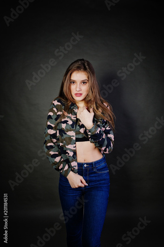 Handsome brunette girl wear military shirt and jeans, posing at studio against gray background. Studio model portrait.