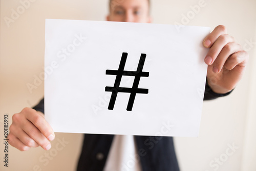 A guy holding a sheet of paper with a hashtag symbol
