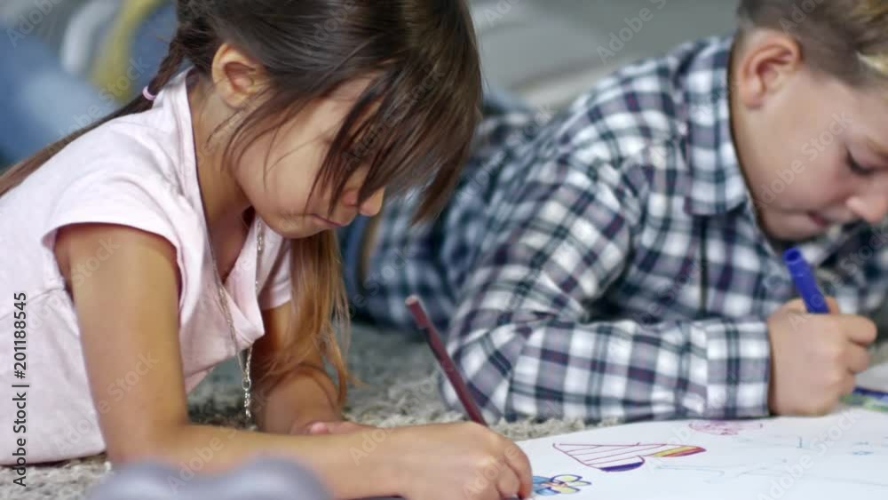 Tracking shot of little girl and boy drawing picture together using colored felt-tip pens and pencils, medium shot Tracking shot of little girl and boy drawing picture together using colored felt-tip pens and pencils, medium shot