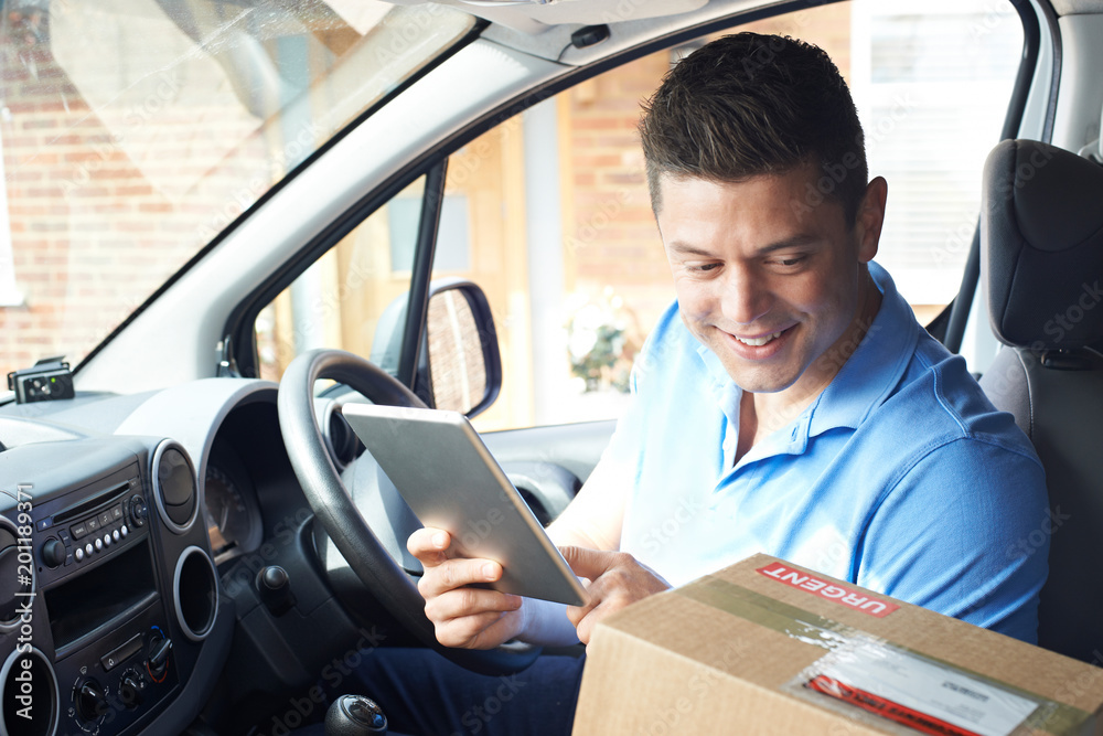 Courier In Van With Digital Tablet Delivering Package To House