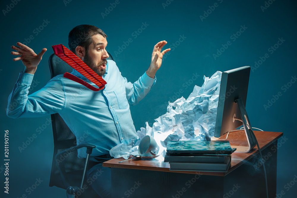 Young stressed handsome businessman working at desk in modern office shouting at laptop screen and being angry about spam - obrazy, fototapety, plakaty 