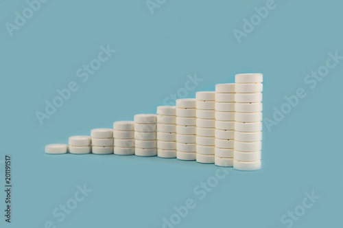 Columns with white round tablets, exposed in the form of an ascending chart on a blue background.