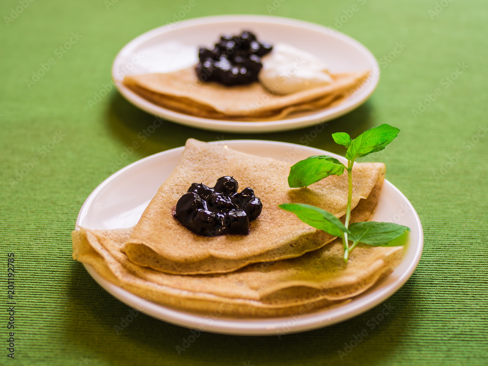Two servings of folded pancakes on a plate with jam and sour cream Two servings of folded pancakes on a plate with jam and sour cream