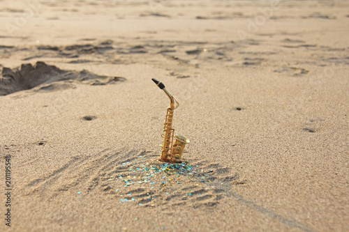 Canvas Print The golden alto saxophone stands on the sand against the background of blue shimmers