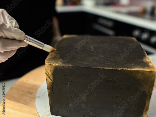 Step-by-step preparation of black designer cake. The confectioner decorates a black cake, gold food paint.