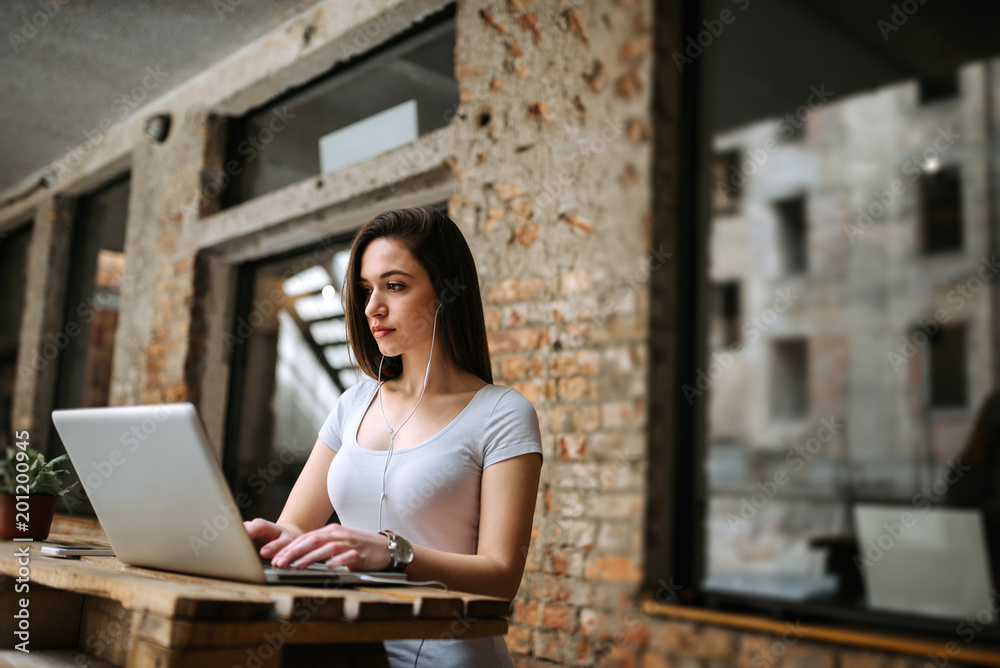 Image of a young woman typing on laptop while listening music on earphones. Online business concept. Image of a young woman typing on laptop while listening music on earphones. Online business concept.