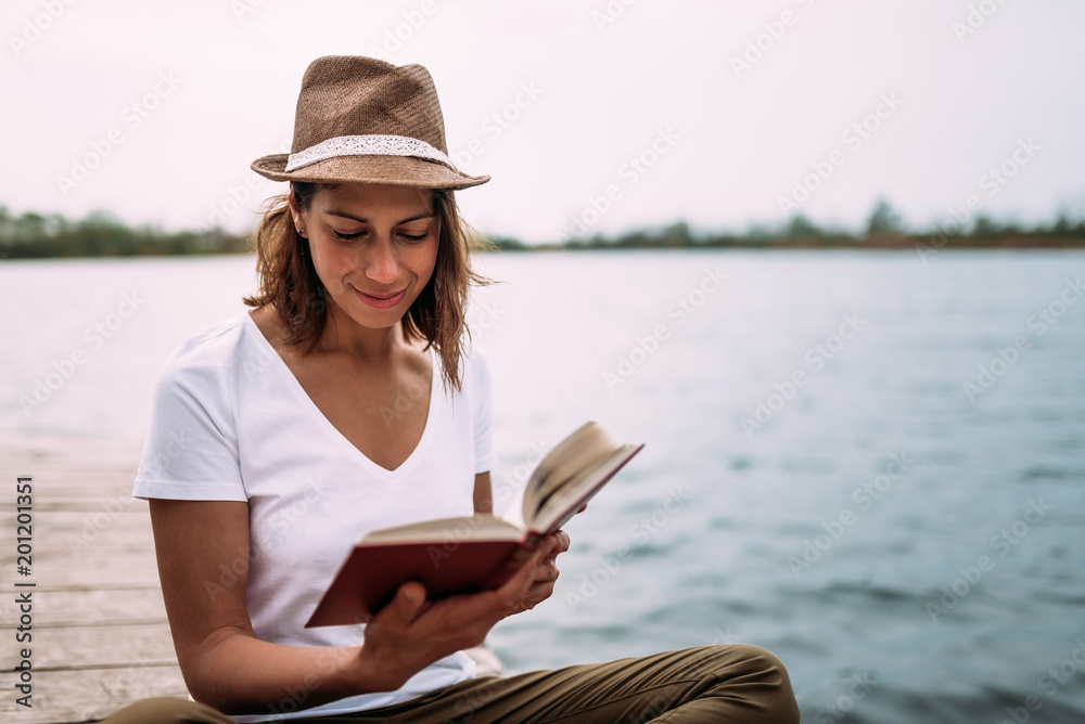 Young female student reading book while sitting near water.