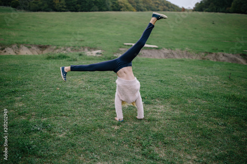 blonde girl performing somersault in park. girl doing exercise outdoors photo