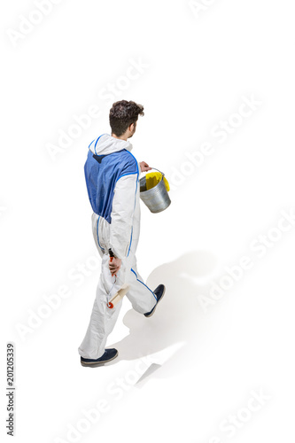 Young male decorator painting with a paint roller climbed a ladder isolated on white background.