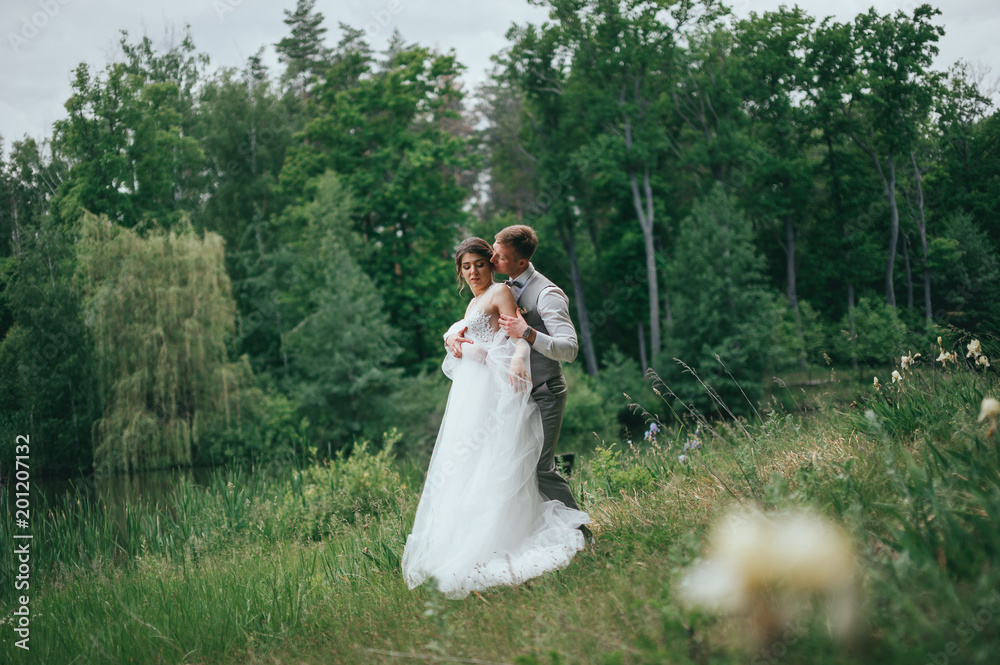 Happy stylish bride and groom walking on the river, smiling and kissing Happy stylish bride and groom walking on the river, smiling and kissing