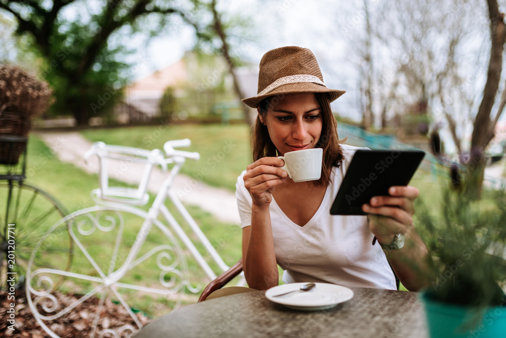 Attractive woman in cafe garden drinking coffee and using tablet. Attractive woman in cafe garden drinking coffee and using tablet.