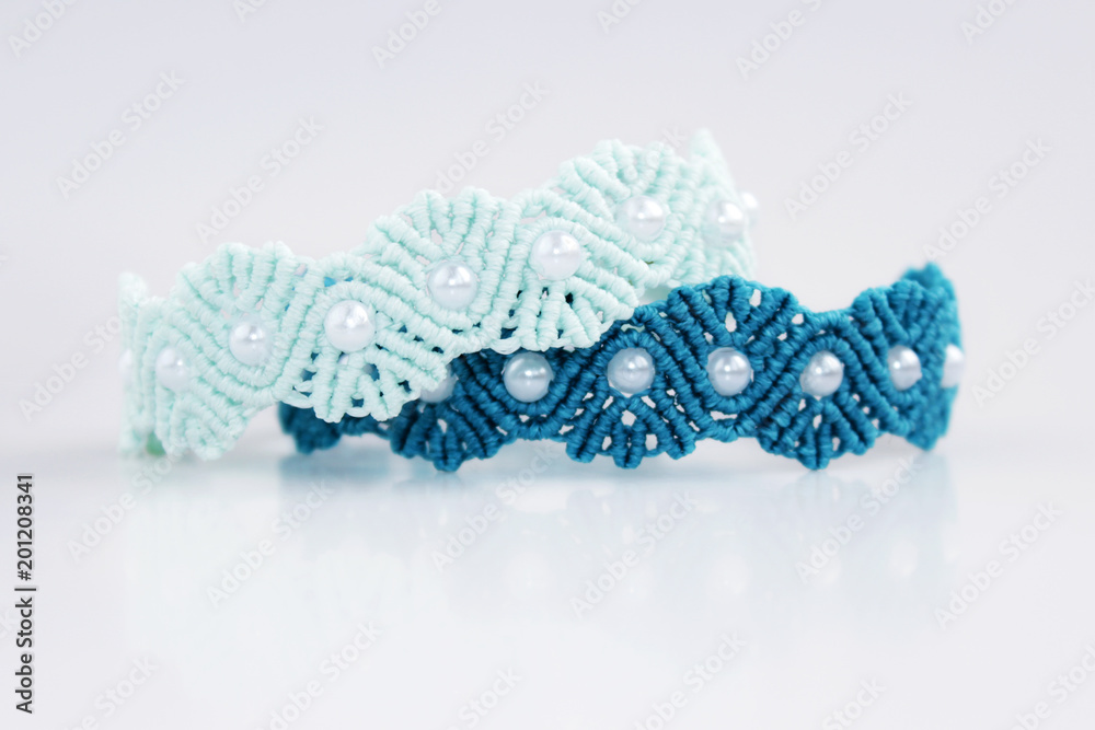 turquoise and blue braceletes with white beads for the hand from waxed thread in the technique of macrame on a white background turquoise and blue braceletes with white beads for the hand from waxed thread in the technique of macrame on a white background
