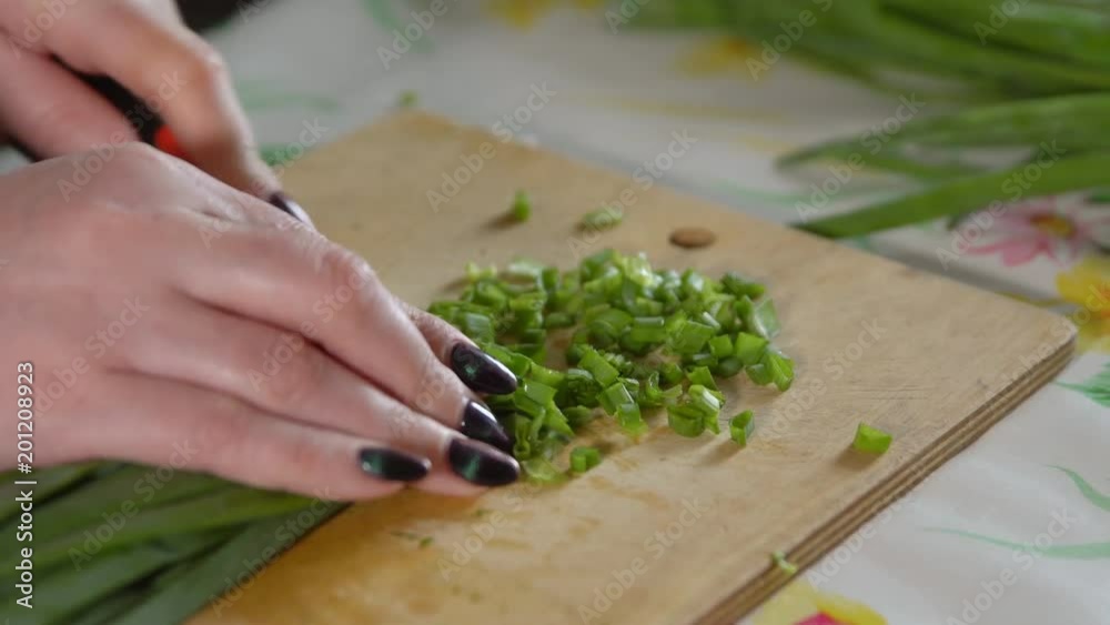 Woman chopping green onions on a wooden cutting board. Woman chopping green onions on a wooden cutting board.