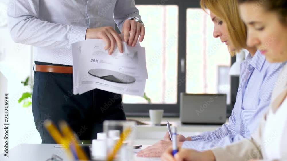 business, corporate and people concept - businessman showing papers with charts to businesswomen at office meeting or presentation business, corporate and people concept - businessman showing papers with charts to businesswomen at office meeting or presentation