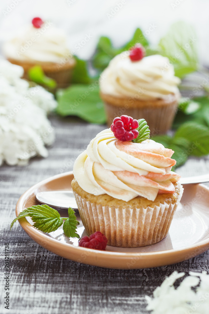 Delicate vanilla cupcakes with cream and raspberries on a dark wooden background Delicate vanilla cupcakes with cream and raspberries on a dark wooden background