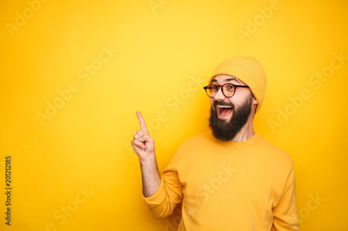 Excited hipster pointing up on yellow