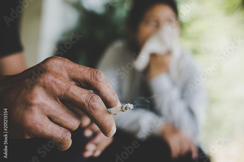 Image of cigarette is in the hand of man in the park.
