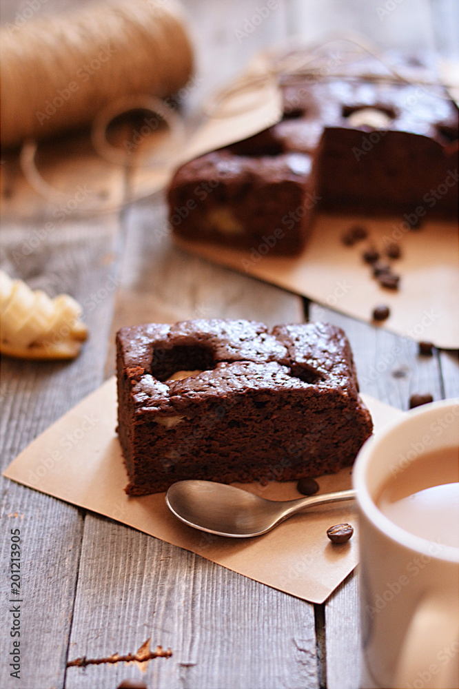 A fresh piece of brownie lies on the table with a Cup of cocoa and a spoon A fresh piece of brownie lies on the table with a Cup of cocoa and a spoon