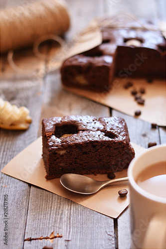 A fresh piece of brownie lies on the table with a Cup of cocoa and a spoon