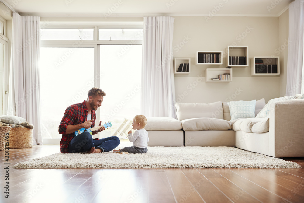 Father playing ukulele with young son in their sitting room Father playing ukulele with young son in their sitting room