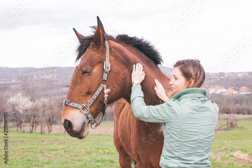 Beautiful young woman on the ranch bonding with a brown horse. 