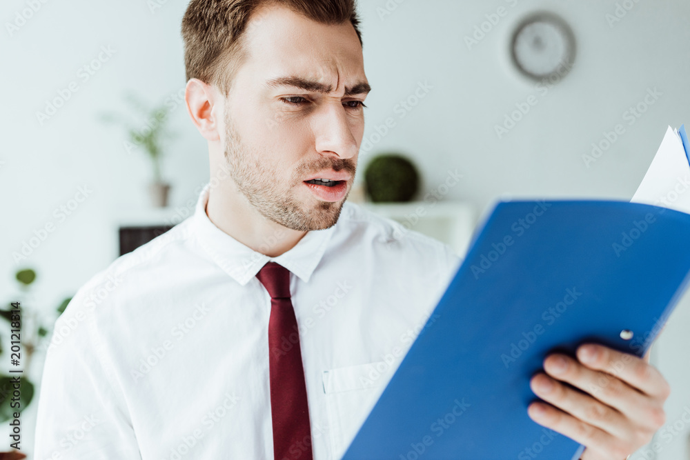 confused businessman holding folder and looking at documents