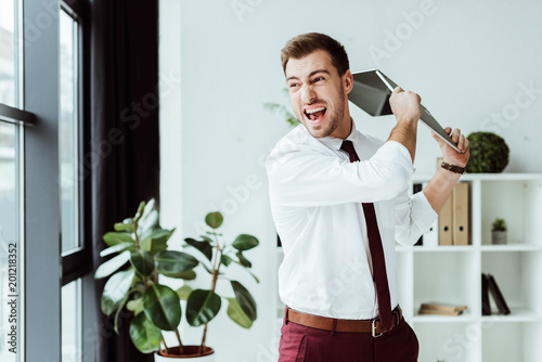 aggressive businessman screaming and throwing laptop in modern office