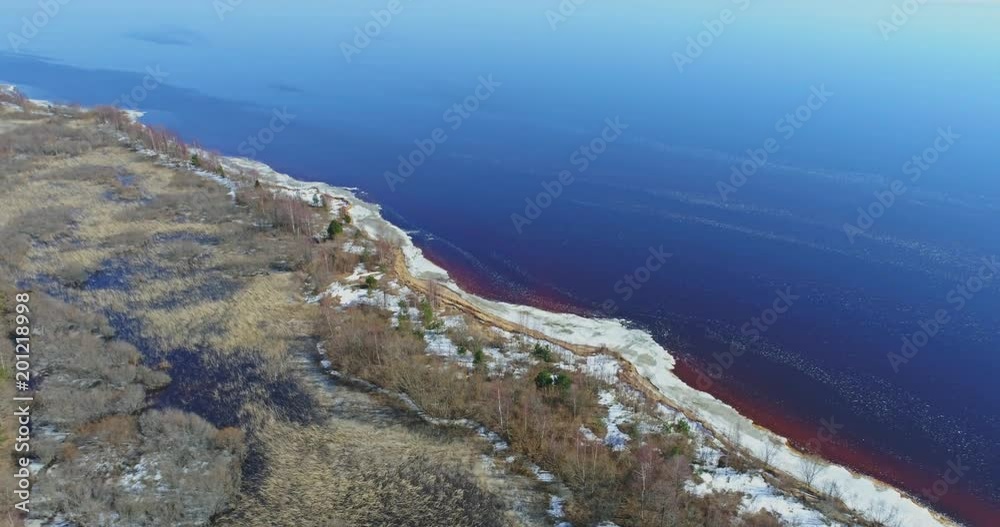 Aerial View Flight over the beach coast, melting ice. Aerial view over sandy coast, lake, forest and snow.
