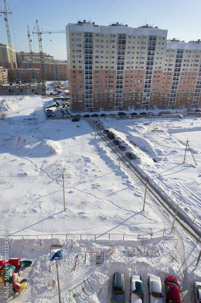 Obraz premium new high-rise building next to the snow-covered field under the blue sky and the sun.