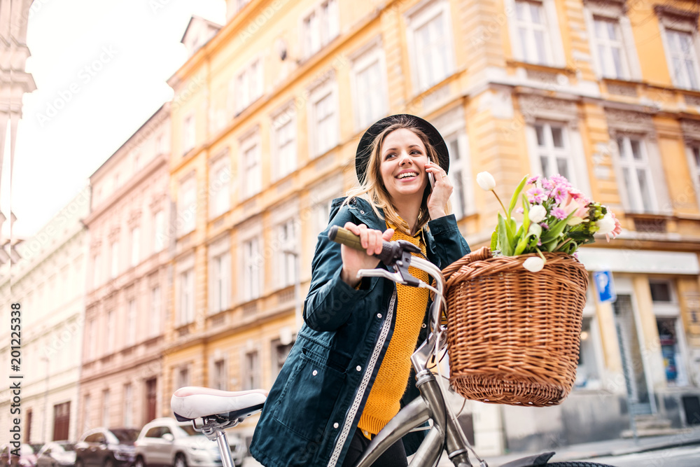 Naklejka premium Young woman with bicycle and smartphone in sunny spring town.