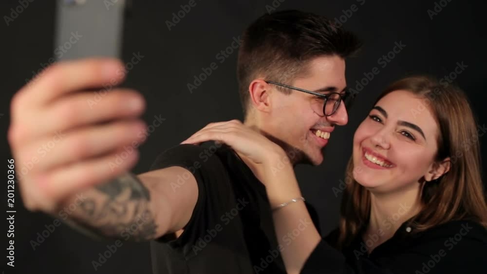 Portrait of two happy lovers making selfie on smartphone on black background. Happy hipster couple taking a selfie on black background. Portrait of two happy lovers making selfie on smartphone on black background. Happy hipster couple taking a selfie on black background.