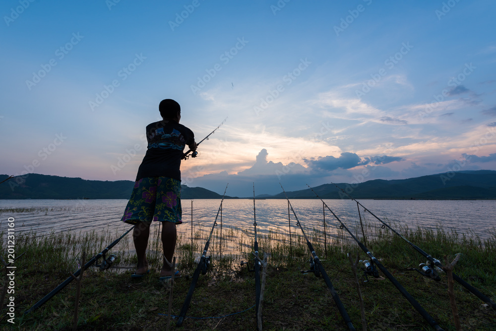 Fisherman fishing near lake on sunset