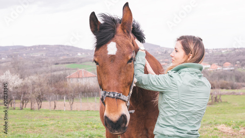 Beautiful young woman on the ranch bonding with a brown horse