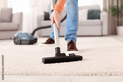 Young man cleaning carpet with vacuum at home