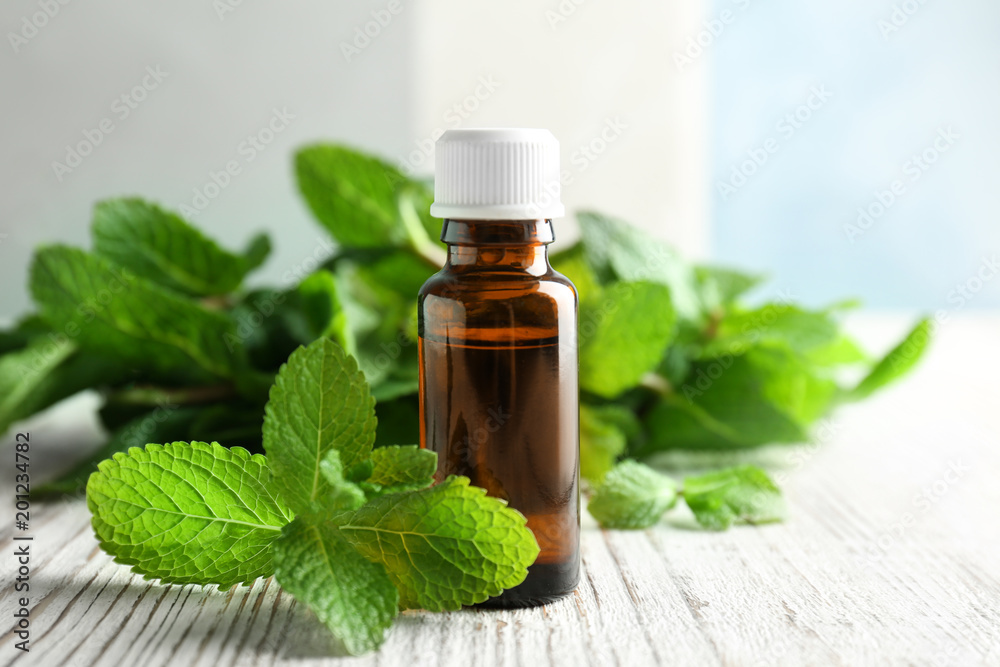 Bottle of essential oil with mint leaves on wooden table Bottle of essential oil with mint leaves on wooden table