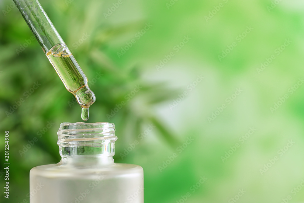 Dripping of essential oil into bottle on blurred background Dripping of essential oil into bottle on blurred background
