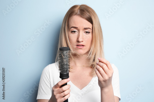Young woman with hair loss problem on color background