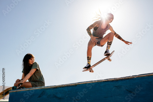 Woman skateboarding at park with friend sitting on ramp