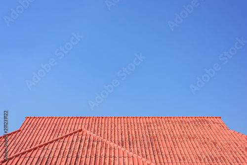 Red roof house with tiled roof on blue sky.