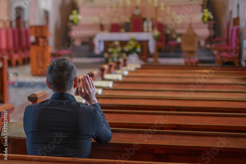 Photo a young man or priest in a black shirt sits on a wooden bench and prays inside t