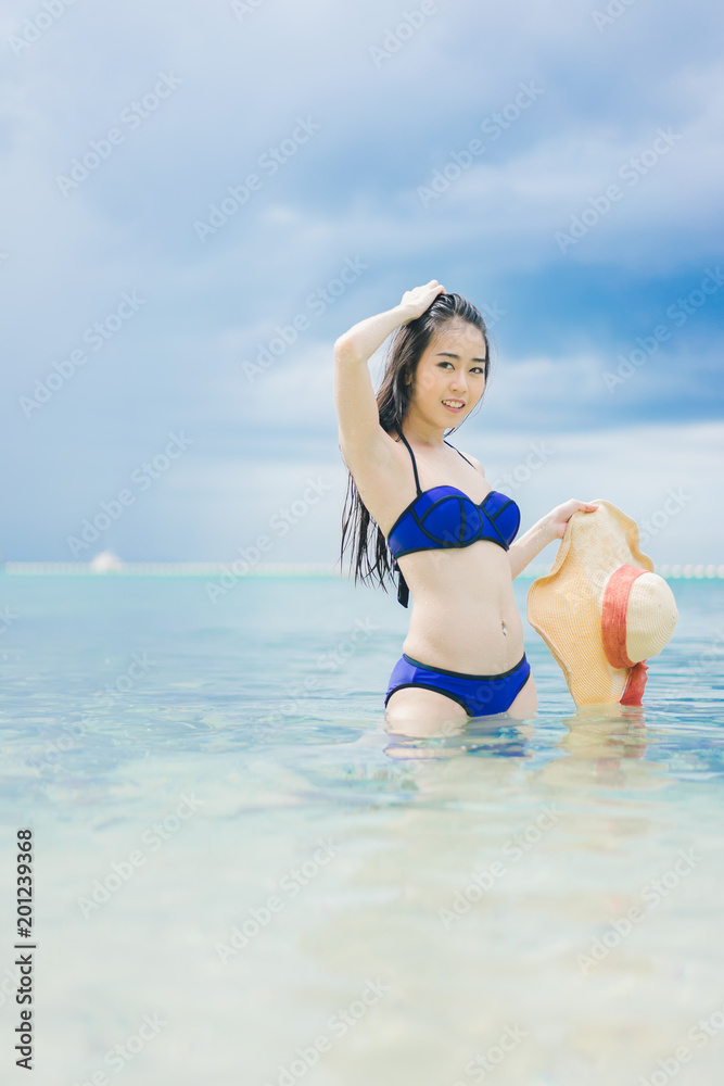 Pretty beautiful asian woman wearing blue swimwear bikini with hat living sunbathing on the beach in the summer