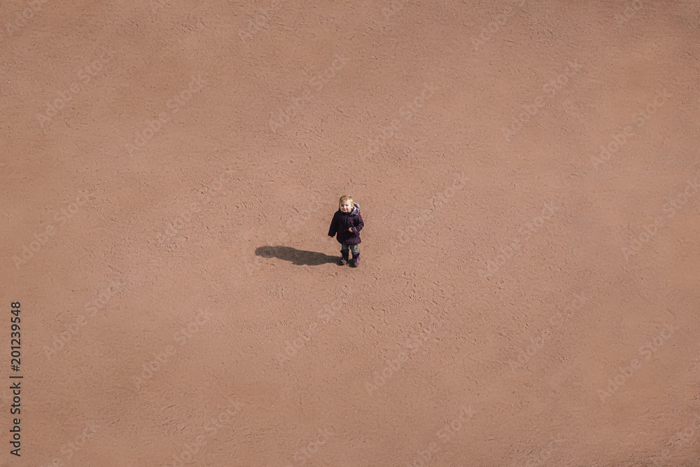 Fototapeta premium small child is standing in the middle of a sandy desert, a conceptual background.