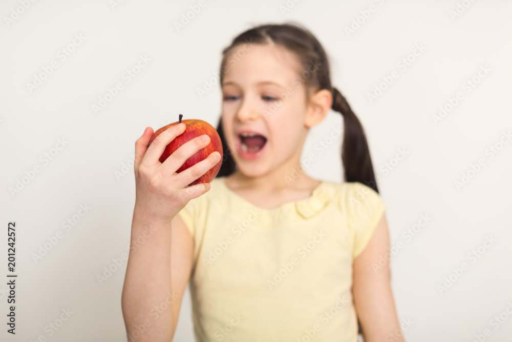 Pretty cute little girl biting red apple over white background