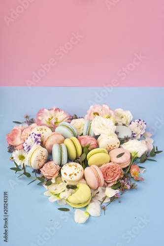 Multi сolored macaroons cakes with big and small different flower buds lay out in the shape of a heart on a blue and pink background photo