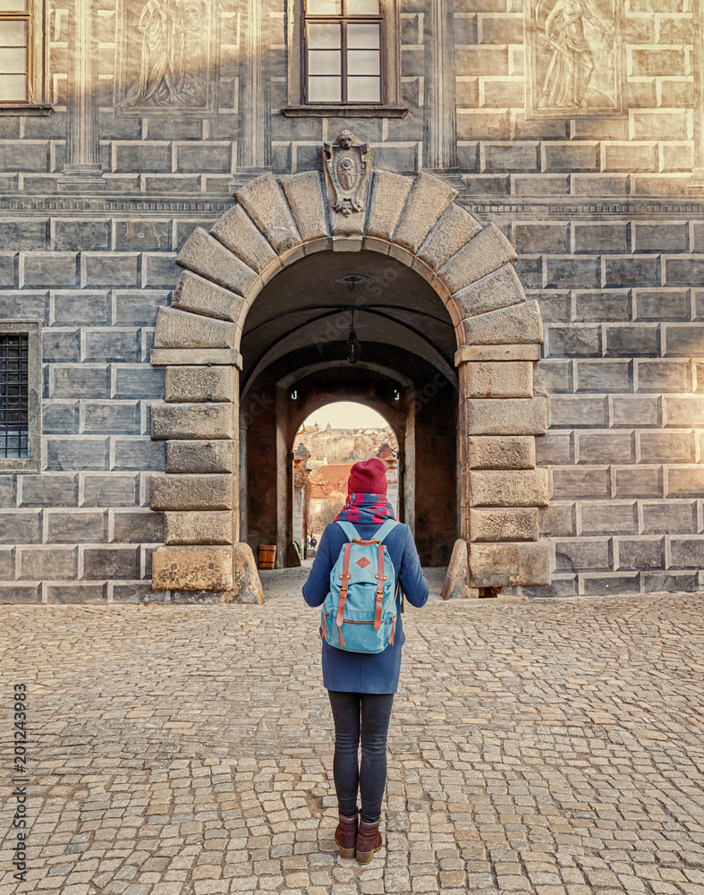 Woman tourist in a coat with a backpack travels at the old streets of Cesky Krumlov city, Europe vacation concept