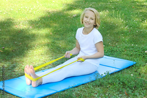 Adorable school aged kid girl playing sports with a rubber band and mat outdoors in the park. Healthy lifestyle. Outdoors workout.