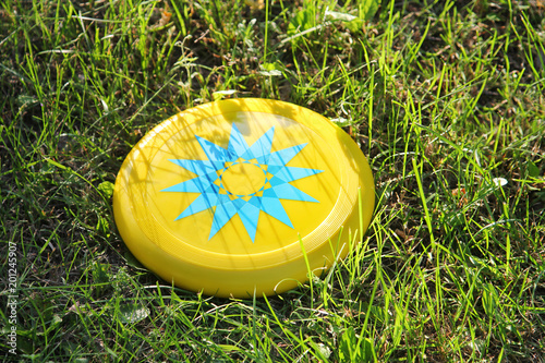 Plastic yellow frisbee flying disc lying in the grass in the park. Children's toy for active outdoor games.